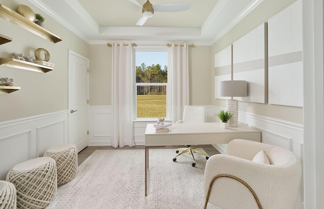 home office with a tray ceiling, a wainscoted wall, wood finished floors, ceiling fan, and ornamental molding