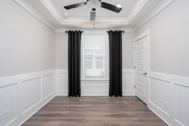 empty room featuring crown molding, a raised ceiling, a wainscoted wall, a ceiling fan, and wood finished floors