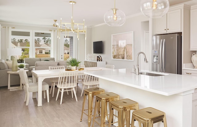 kitchen featuring stainless steel fridge, ornamental molding, a sink, open floor plan, and a kitchen breakfast bar