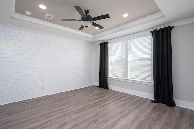 unfurnished room featuring visible vents, wood finished floors, a ceiling fan, and a raised ceiling