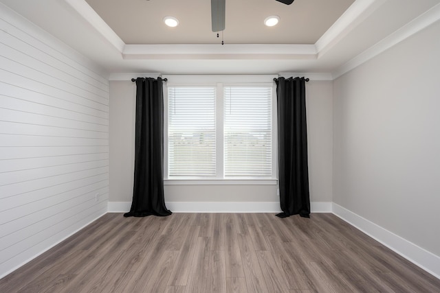 spare room with baseboards, a raised ceiling, wooden walls, a ceiling fan, and wood finished floors