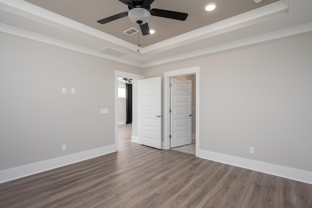 empty room with a ceiling fan, a raised ceiling, wood finished floors, and visible vents