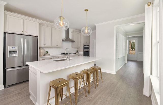 kitchen with tasteful backsplash, a breakfast bar, a sink, wall chimney range hood, and appliances with stainless steel finishes