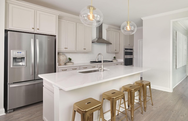 kitchen featuring crown molding, a sink, tasteful backsplash, appliances with stainless steel finishes, and wall chimney range hood