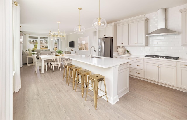 kitchen with stainless steel fridge, a sink, open floor plan, a breakfast bar area, and wall chimney range hood