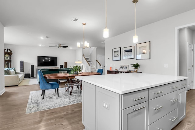 kitchen with a center island, pendant lighting, gray cabinets, ceiling fan with notable chandelier, and light wood-type flooring