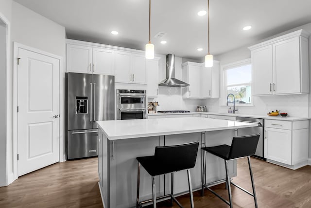 kitchen with a center island, white cabinets, wall chimney range hood, and appliances with stainless steel finishes