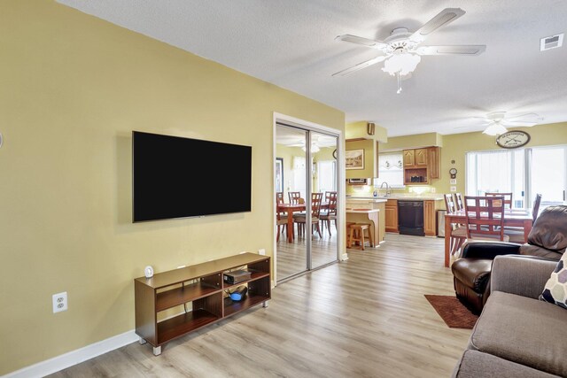 living room with ceiling fan, sink, light wood-type flooring, and a textured ceiling