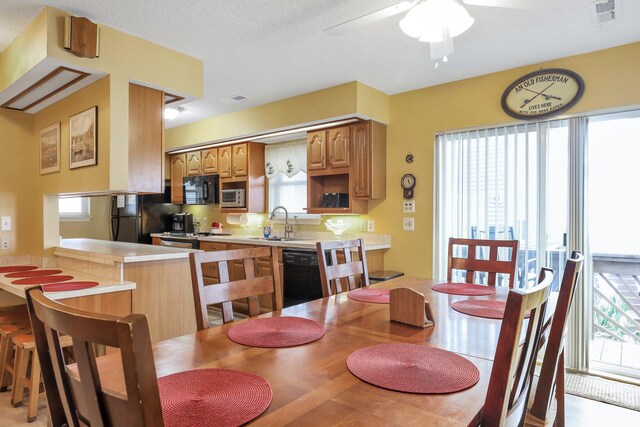 kitchen featuring sink, kitchen peninsula, light hardwood / wood-style floors, a breakfast bar, and black appliances