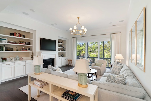 living area with crown molding, a glass covered fireplace, dark wood-type flooring, a chandelier, and built in shelves