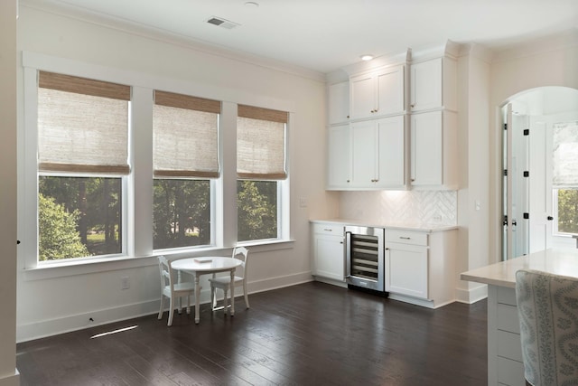 bar featuring arched walkways, dark wood-type flooring, wine cooler, visible vents, and ornamental molding