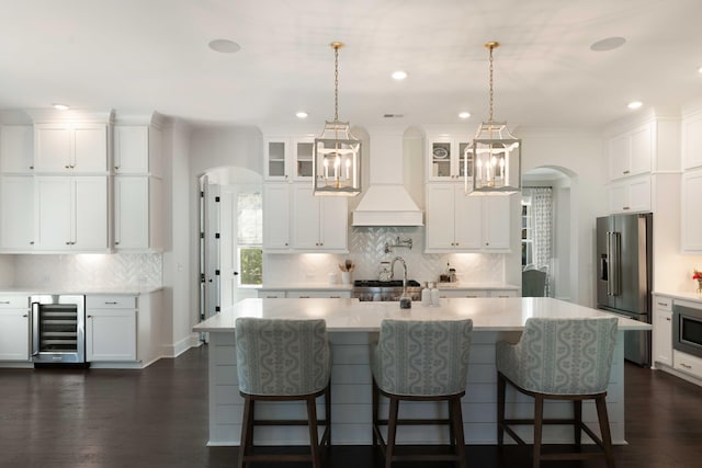kitchen featuring appliances with stainless steel finishes, arched walkways, a sink, custom exhaust hood, and beverage cooler
