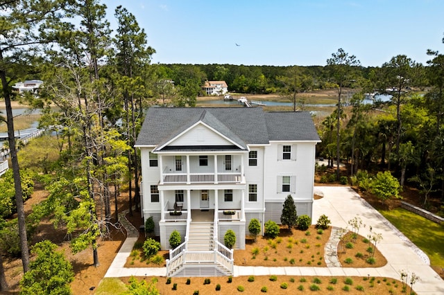 coastal home with a balcony, roof with shingles, stairs, a porch, and driveway