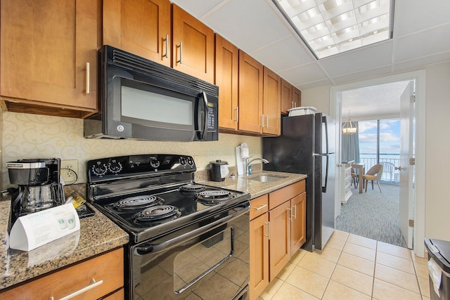 kitchen featuring sink, black appliances, light tile patterned floors, dark stone counters, and a drop ceiling