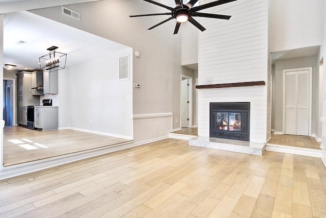 1052 Yorktown Dr, Charleston, SC 29412 - unfurnished living room with ceiling fan, a towering ceiling, light wood-style flooring, a fireplace, and a chandelier