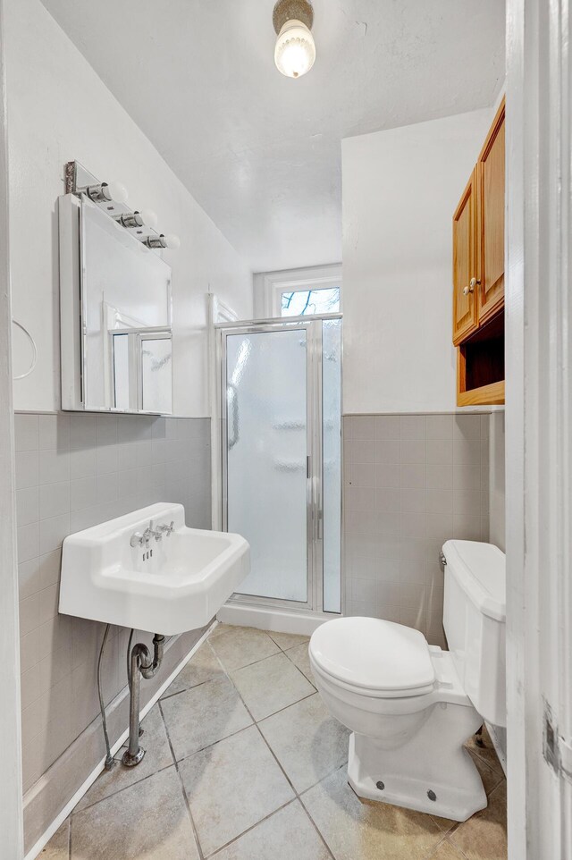 bathroom featuring tile walls, toilet, a sink, a shower stall, and tile patterned floors