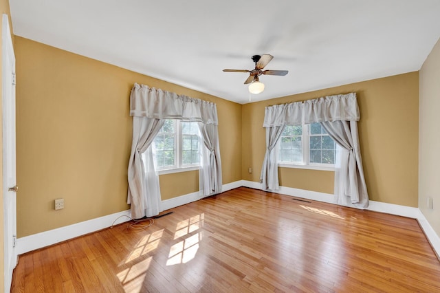 unfurnished room featuring ceiling fan, wood finished floors, baseboards, and a healthy amount of sunlight