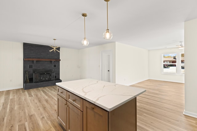 kitchen featuring light wood-type flooring, light stone counters, ceiling fan, a fireplace, and hanging light fixtures