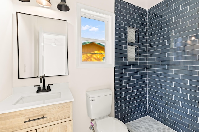 bathroom featuring a tile shower, vanity, and toilet