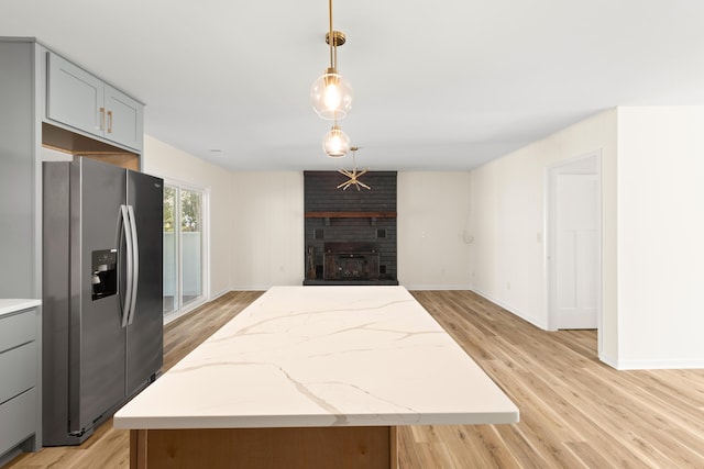 kitchen with stainless steel refrigerator with ice dispenser, gray cabinetry, pendant lighting, light hardwood / wood-style flooring, and a kitchen island