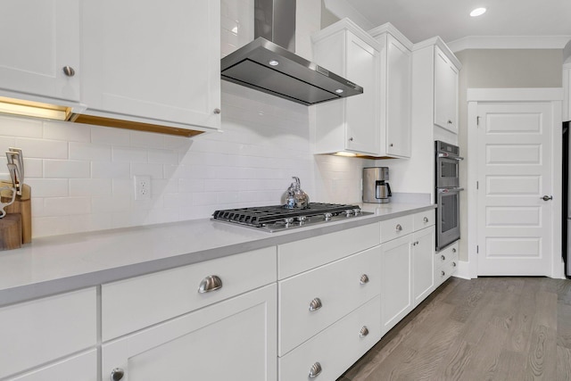 kitchen with wall chimney exhaust hood, white cabinetry, tasteful backsplash, appliances with stainless steel finishes, and hardwood / wood-style flooring