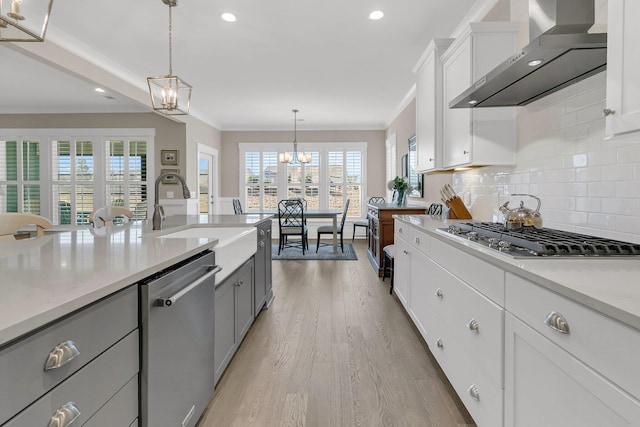 kitchen with wall chimney range hood, white cabinetry, an inviting chandelier, stainless steel appliances, and decorative light fixtures