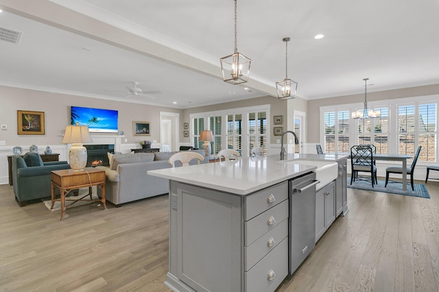 kitchen with gray cabinetry, decorative light fixtures, light hardwood / wood-style flooring, stainless steel dishwasher, and an island with sink