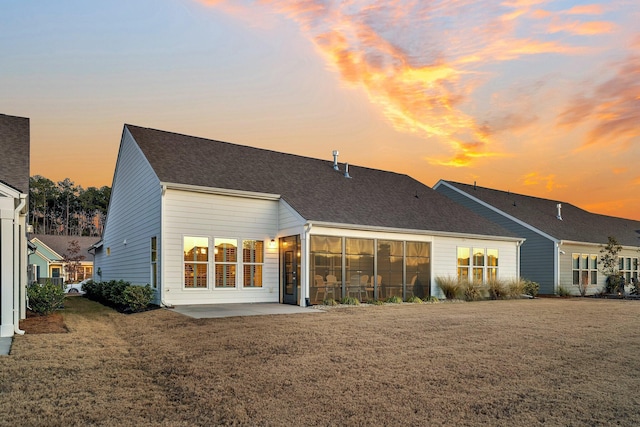 back house at dusk featuring a yard and a patio