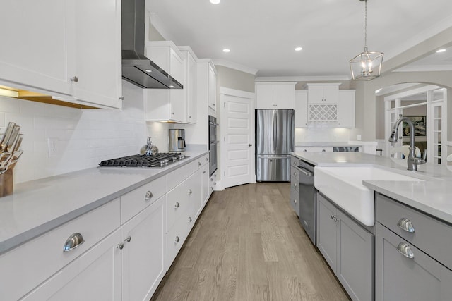 kitchen featuring pendant lighting, wall chimney range hood, sink, stainless steel appliances, and white cabinets