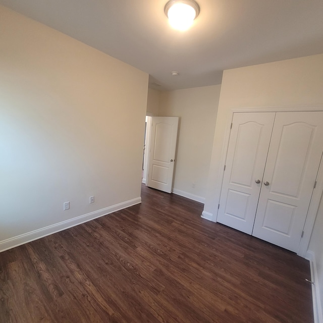 unfurnished bedroom featuring baseboards, dark wood finished floors, and a closet