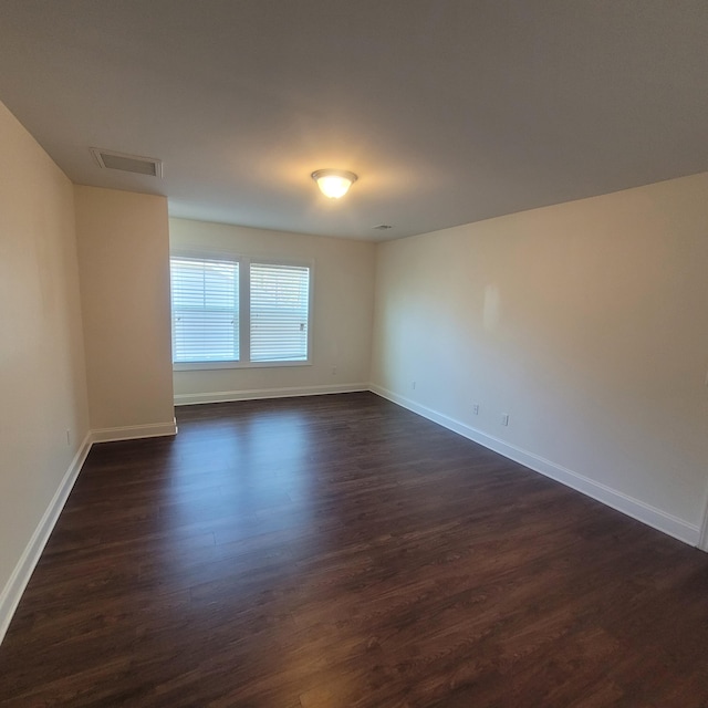 spare room with dark wood-type flooring, visible vents, and baseboards