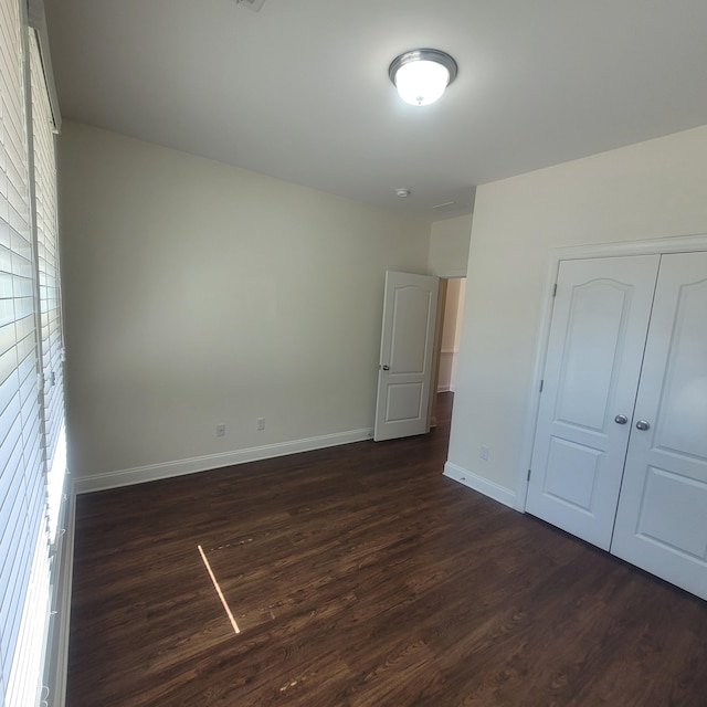 unfurnished bedroom featuring dark wood-style floors, a closet, and baseboards