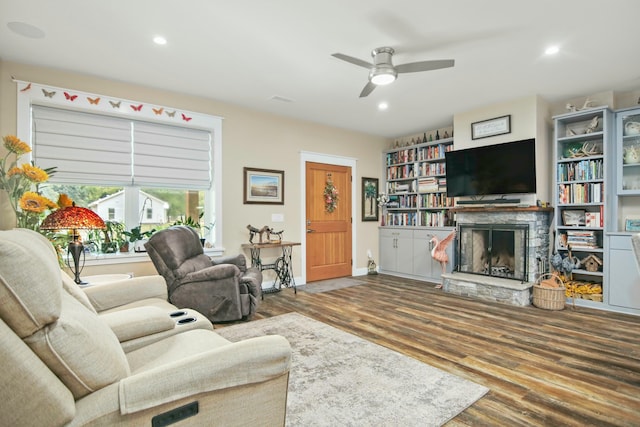 living room featuring hardwood / wood-style flooring, a stone fireplace, and ceiling fan