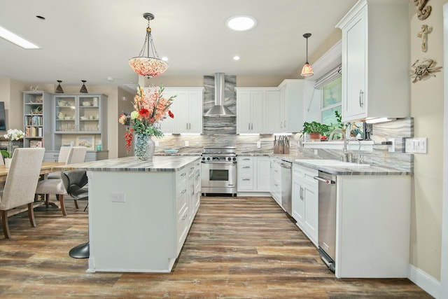 kitchen featuring stainless steel appliances, white cabinetry, hanging light fixtures, and wall chimney exhaust hood