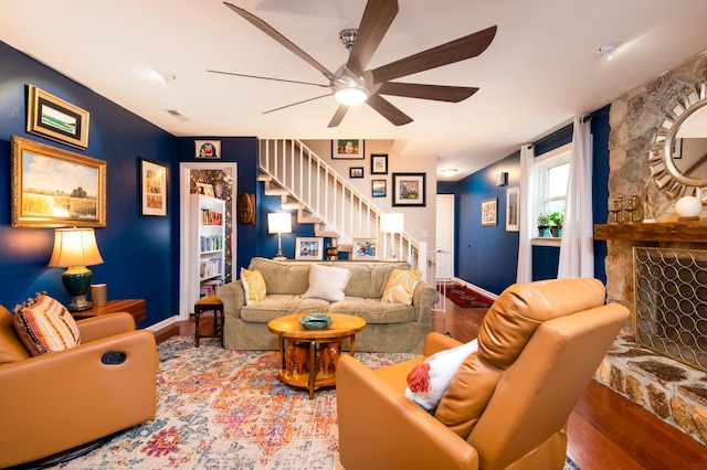 living room featuring hardwood / wood-style floors, a stone fireplace, and ceiling fan