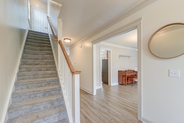 stairway with crown molding, wood finished floors, and baseboards