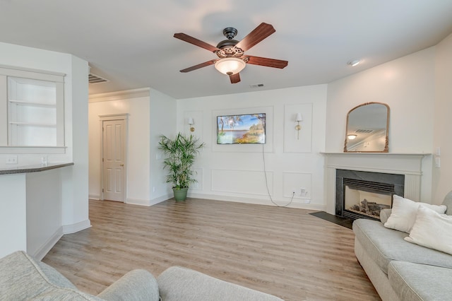 living room with a ceiling fan, a fireplace with flush hearth, light wood finished floors, and baseboards