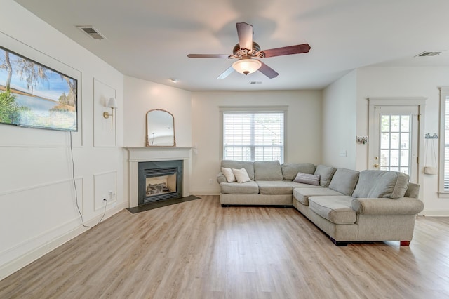 living area featuring light wood-type flooring, a fireplace with flush hearth, a ceiling fan, and baseboards