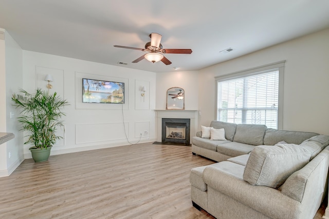 living area with ceiling fan, light wood finished floors, a fireplace with flush hearth, and baseboards