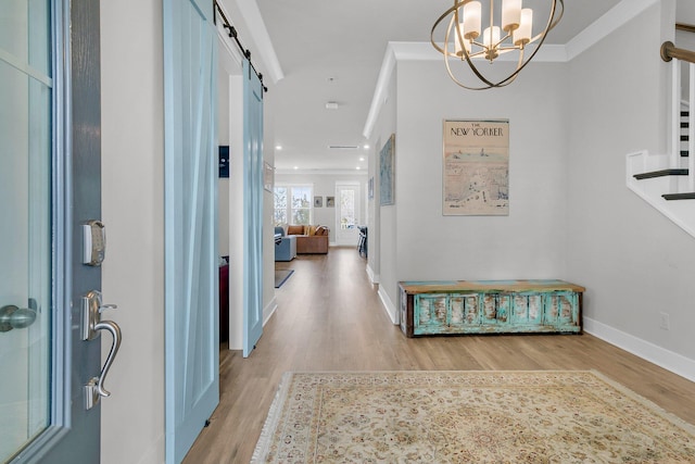 hallway featuring light hardwood / wood-style floors, a barn door, ornamental molding, and a chandelier