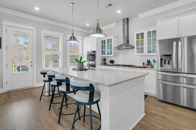 kitchen featuring white cabinetry, stainless steel appliances, wall chimney range hood, tasteful backsplash, and a center island with sink