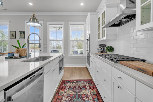 kitchen with appliances with stainless steel finishes, tasteful backsplash, wall chimney exhaust hood, sink, and white cabinets