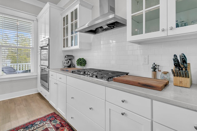 kitchen featuring decorative backsplash, appliances with stainless steel finishes, white cabinetry, and wall chimney exhaust hood