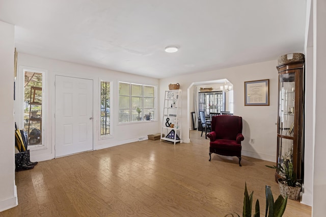 foyer entrance with arched walkways, a healthy amount of sunlight, an inviting chandelier, and wood finished floors