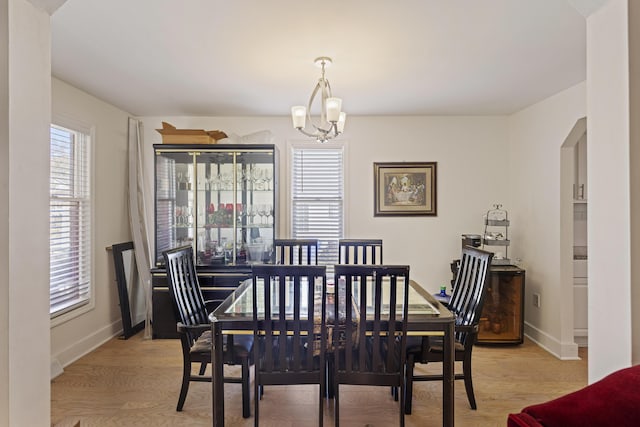 dining area featuring baseboards, arched walkways, a notable chandelier, and light wood-style flooring