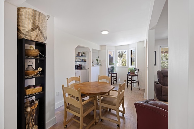 dining space featuring baseboards, arched walkways, and wood finished floors