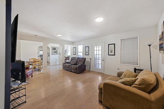 living room featuring light wood-style flooring, arched walkways, and baseboards