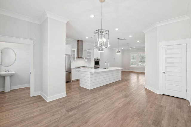 kitchen featuring a sink, appliances with stainless steel finishes, wall chimney exhaust hood, a center island with sink, and crown molding