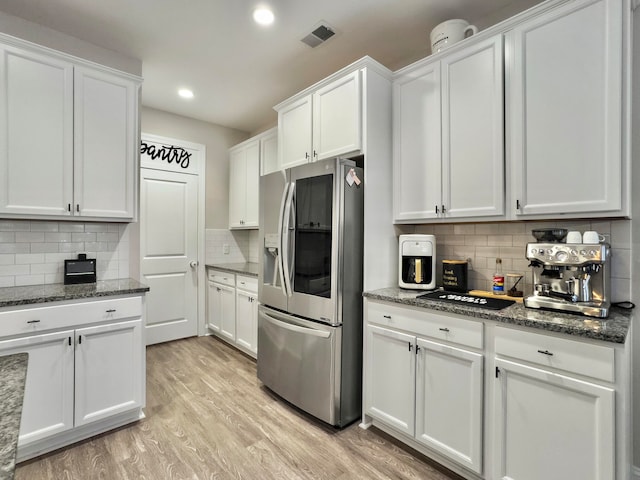 kitchen featuring white cabinets, stainless steel fridge, light hardwood / wood-style flooring, dark stone counters, and decorative backsplash