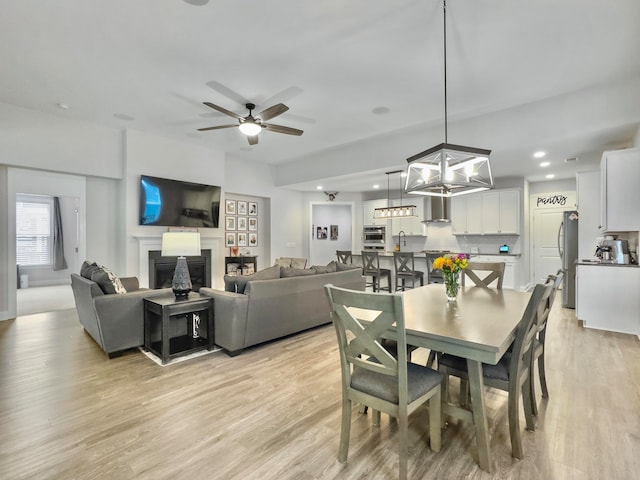 dining space with sink, ceiling fan with notable chandelier, and light hardwood / wood-style floors